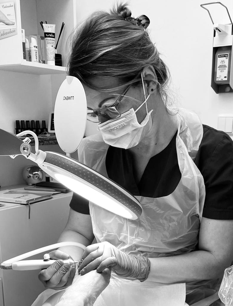 Nancy behandelt een voet onder de lamp, met mondkapje en handschoenen